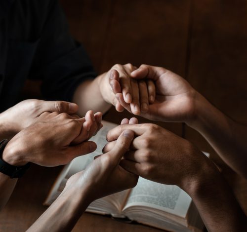 A group of young Christians holding hands in prayer for faith and scriptures