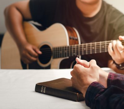 Young men play the guitar, praise God with music, and worship God together in a Christian family.